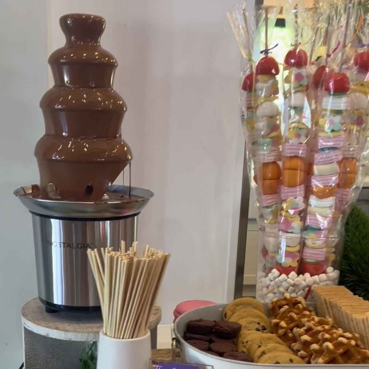 Chocolate fountain with dipping sticks and assorted candies in the background