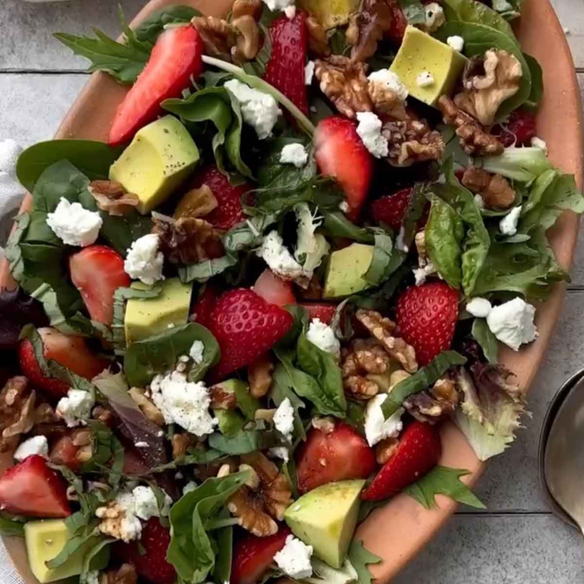 Salad with strawberries, avocados, walnuts, and blue cheese on a wooden plate.