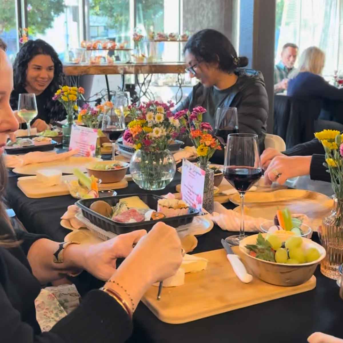 Group of people together at a charcuterie workshop with wine glasses and food.