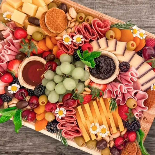 Assorted meats, cheeses, fruits, and vegetables arranged on a wooden board.