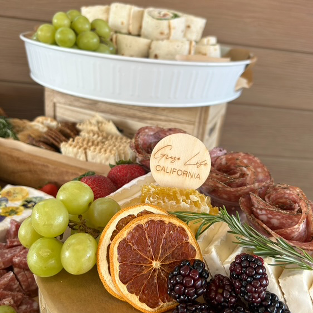 Assorted meats, cheeses, fruits, and bread on a tiered serving tray with 'Graze Life California' branding.