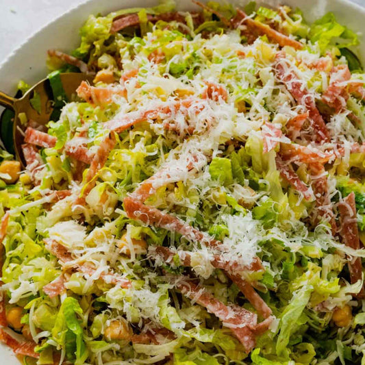 Salad with shredded lettuce, bacon, and grated cheese in a white bowl.