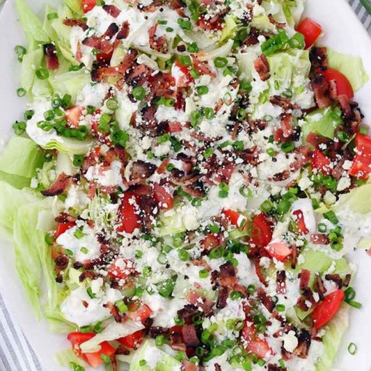 Salad with lettuce, bacon, cheese, and vegetables on a white plate